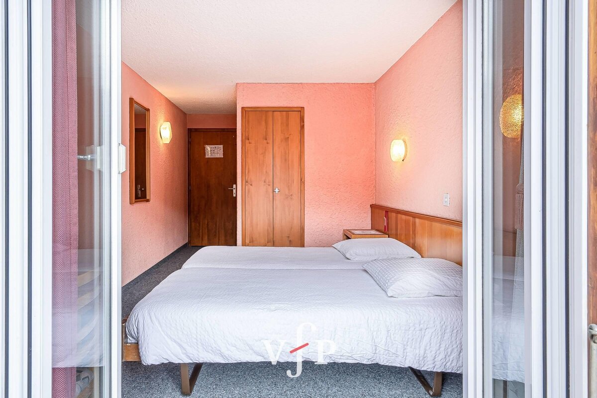 A simple hotel room with pink walls, two beds pushed together, and wooden doors, viewed through sliding glass doors.