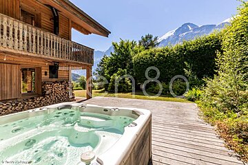 A hot tub sits on a wooden deck in front of a log cabin