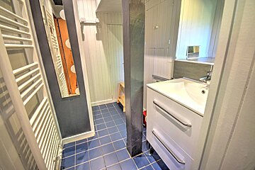 Narrow bathroom featuring a white vanity, blue tiled floor, a grey central pillar, and a white towel warmer.