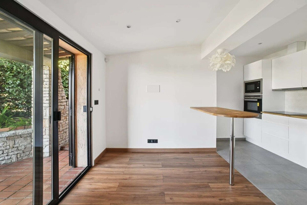 Bright, modern kitchen-living space with white cabinets, wood floors, a bar, and sliding glass doors opening to a patio.