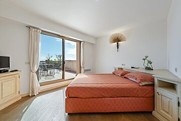 Bright bedroom featuring a coral-orange bed and large sliding glass doors leading to a sunny outdoor terrace.