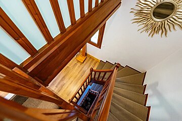 High-angle view down a winding wooden staircase with carpeted steps, wooden railings, and a sunburst mirror on the wall.