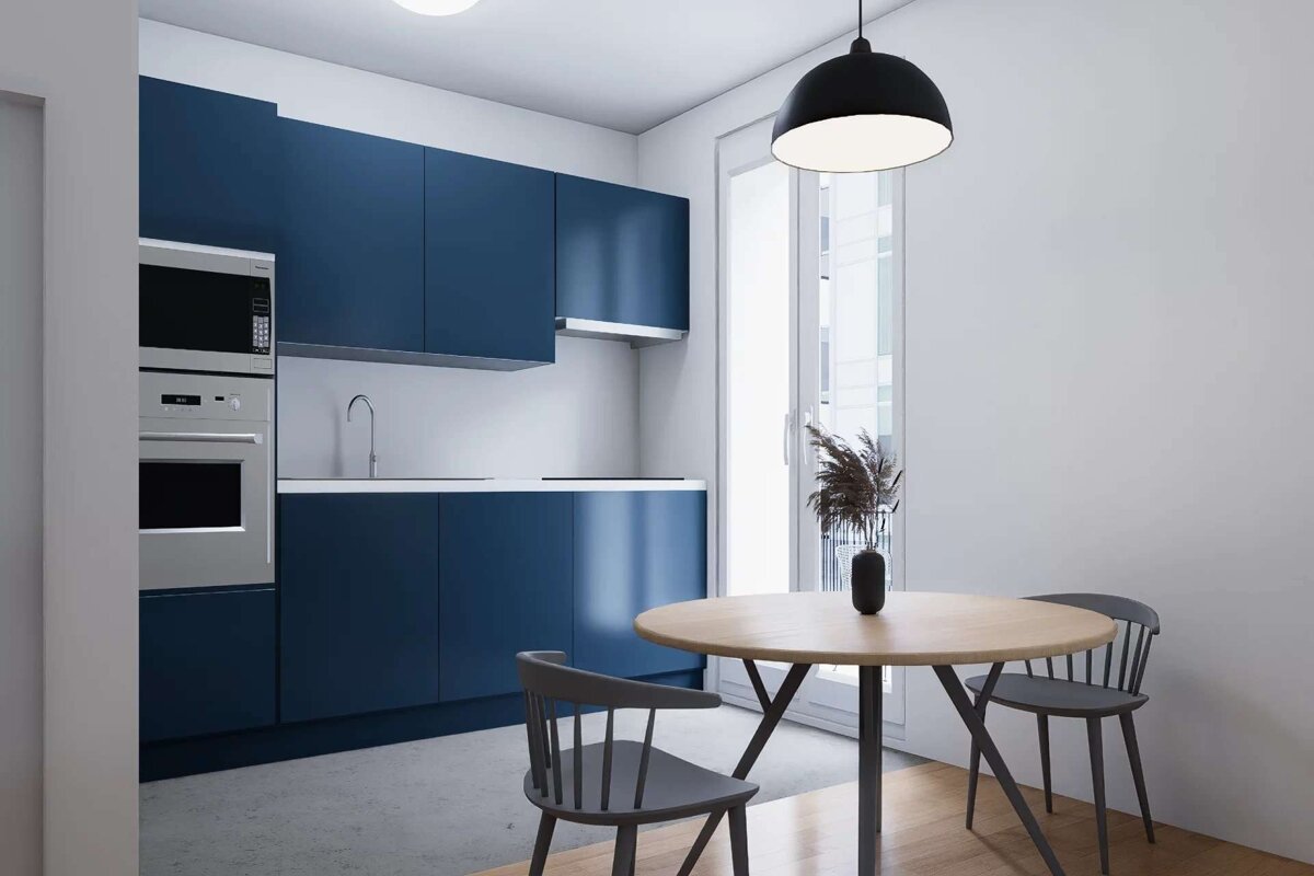 A modern kitchen featuring navy blue cabinets, stainless steel appliances, and a light wood dining table with dark chairs. White walls, a large window, and a black pendant light complete the scene.