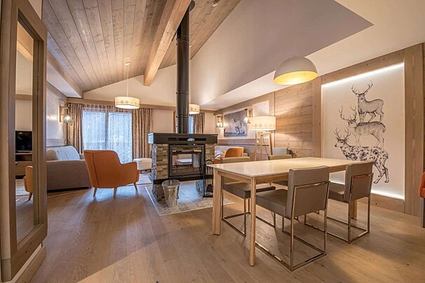A spacious, modern chalet-style living and dining area featuring a central fireplace, vaulted wood ceilings, and deer artwork, creating a warm, contemporary ambiance.