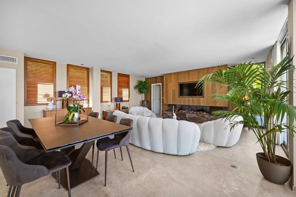 An elegant modern open-plan living and dining room with a large white curved sofa, wood-paneled TV wall, and stylish furniture.