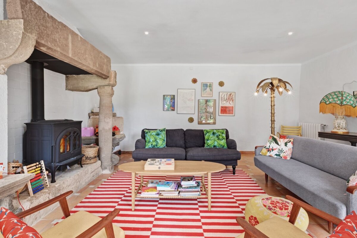 A vibrant, eclectic living room featuring a prominent stone fireplace, a bold red and white striped rug, two sofas, and varied colorful decor.
