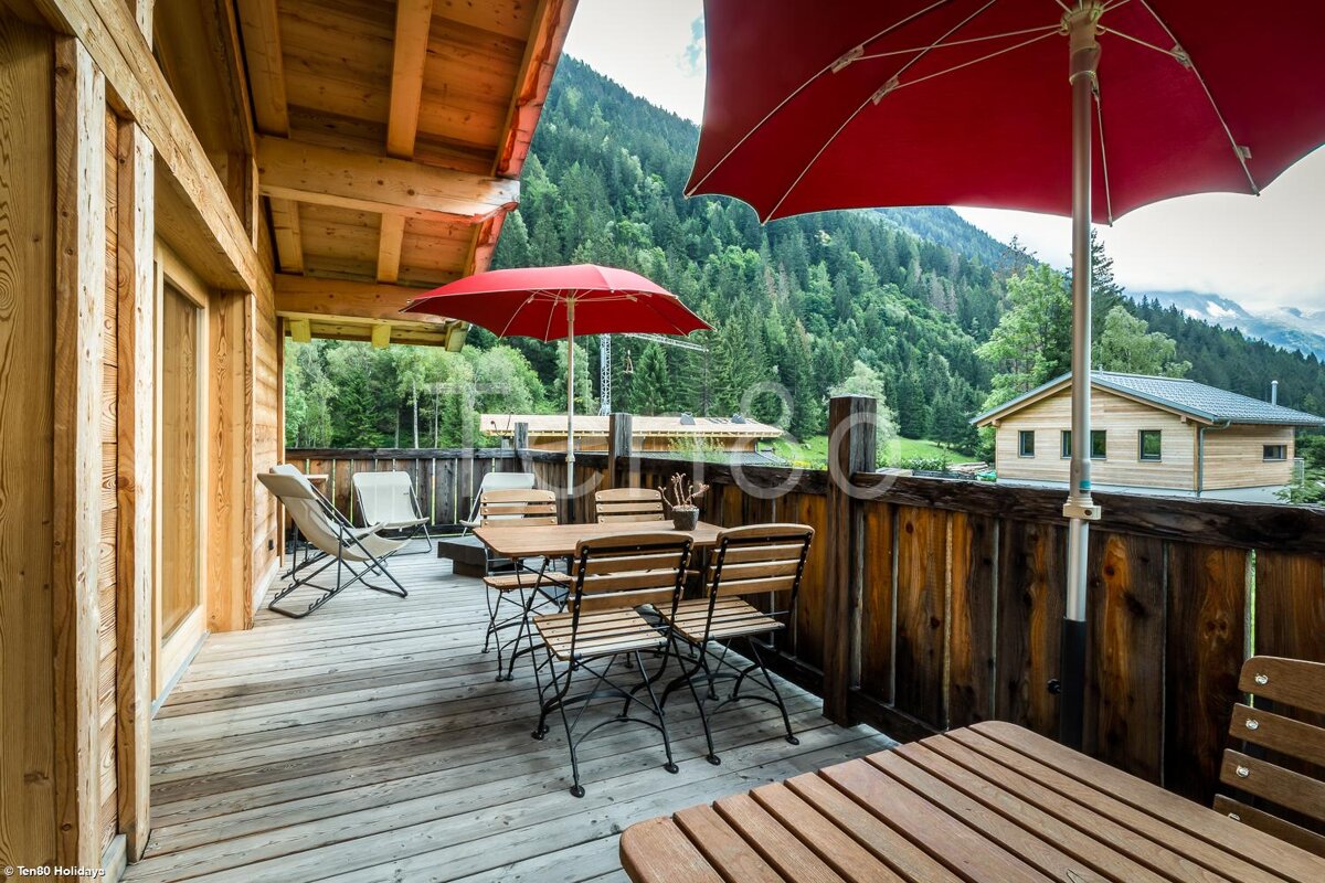 A wooden deck with a table and chairs and a red umbrella