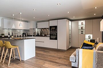Modern open-plan kitchen with white cabinetry, an island with yellow bar stools, and a cozy living area with a grey sofa.