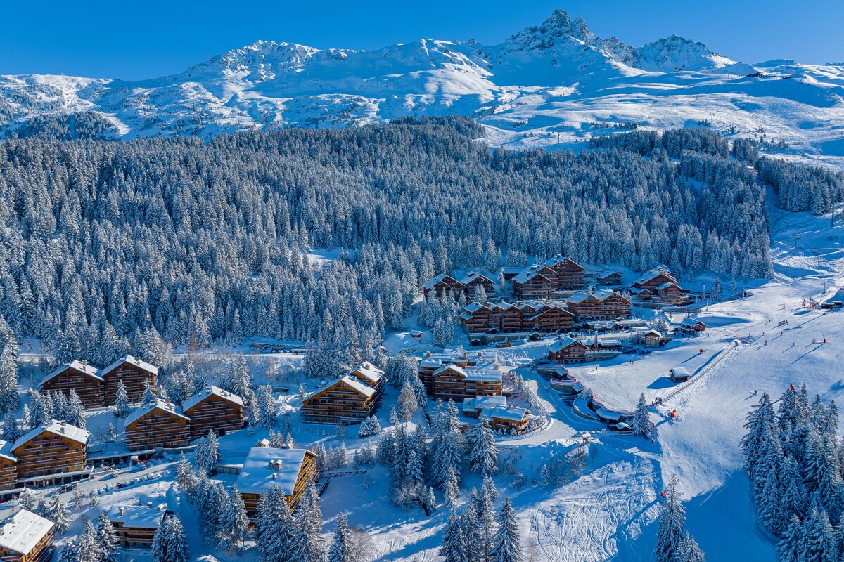 Snowy ski resort with alpine chalets nestled in a dense pine forest under majestic mountains.