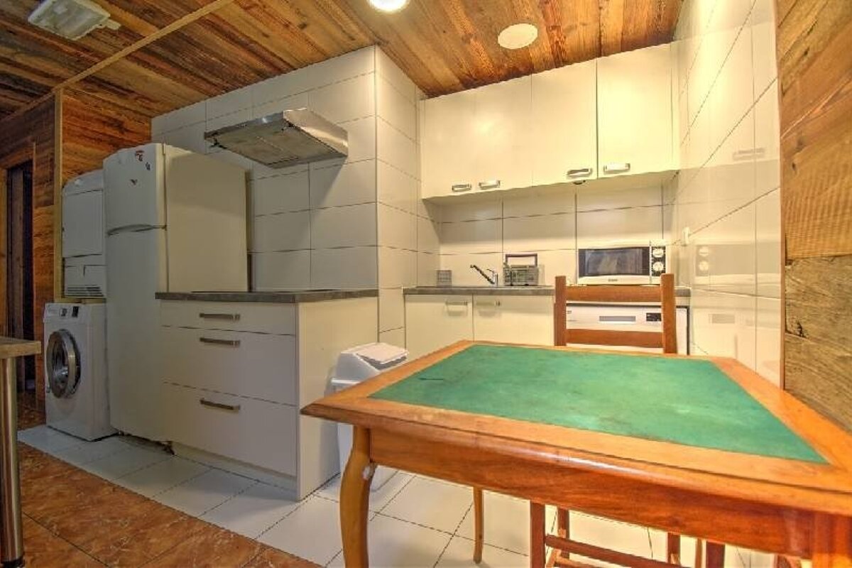 Rustic cabin kitchen with white cabinets, appliances, and a wooden table with a green top in the foreground.
