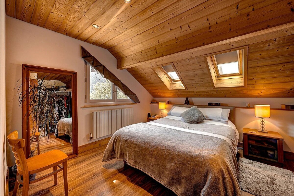 A charming, wood-paneled attic bedroom featuring a double bed, skylights, a large mirror, and a window with a view.