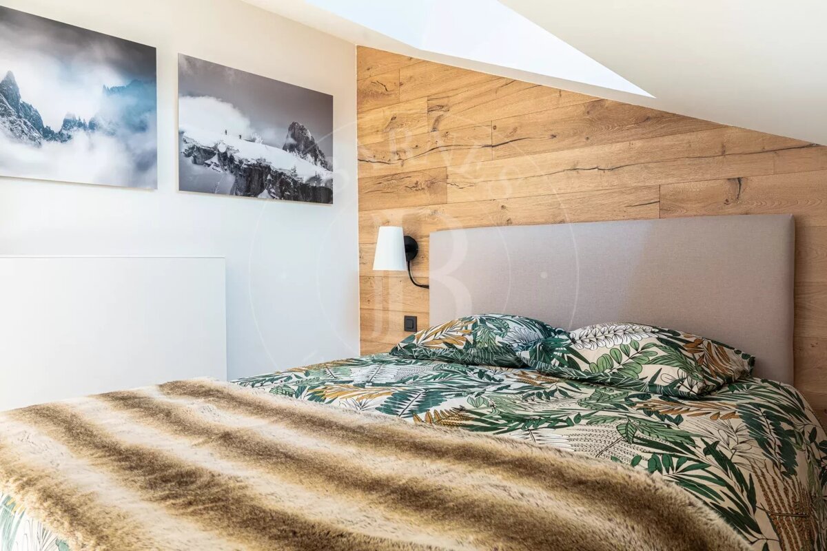 Modern bedroom with a bed featuring botanical print bedding, a fur throw, a wood-paneled accent wall, and two mountain art prints.