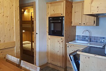 A rustic wooden kitchen featuring pine cabinets, a black oven, and a doorway opening to a bedroom with bunk beds.