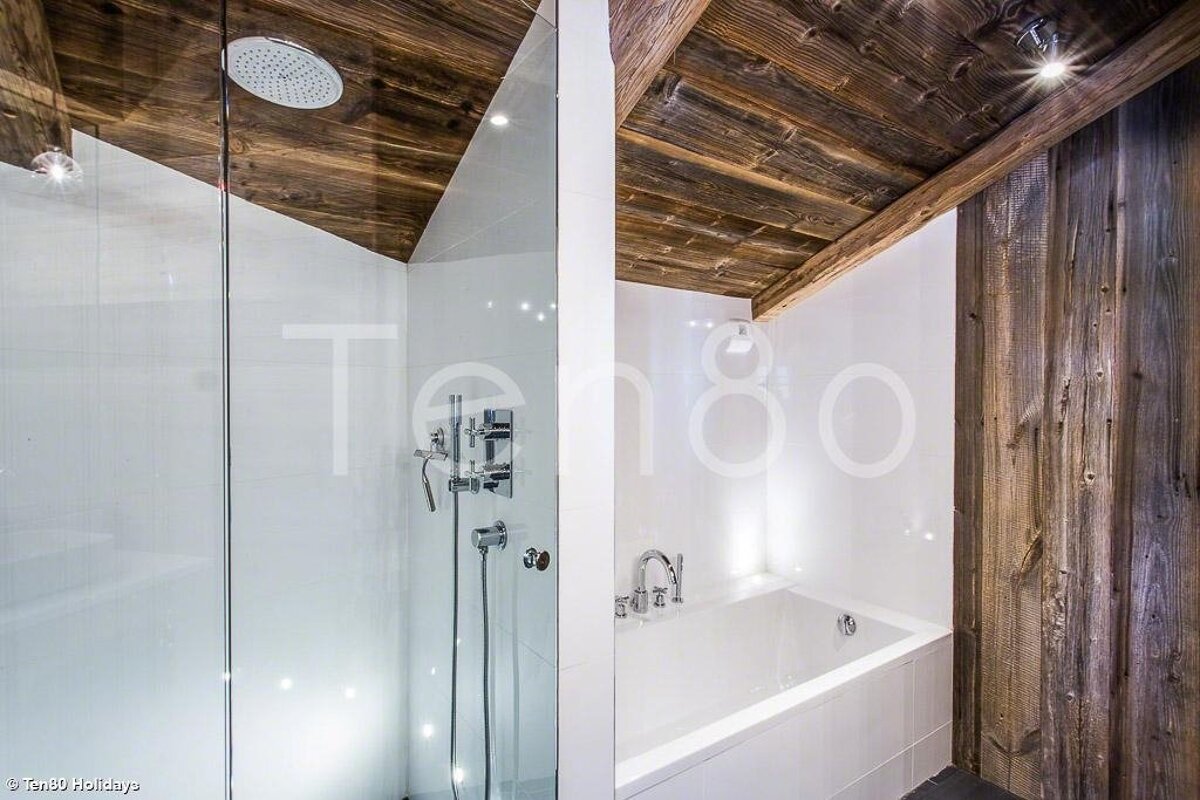 Modern chalet bathroom with a glass-enclosed shower, white bathtub, and rustic vaulted wooden ceiling.