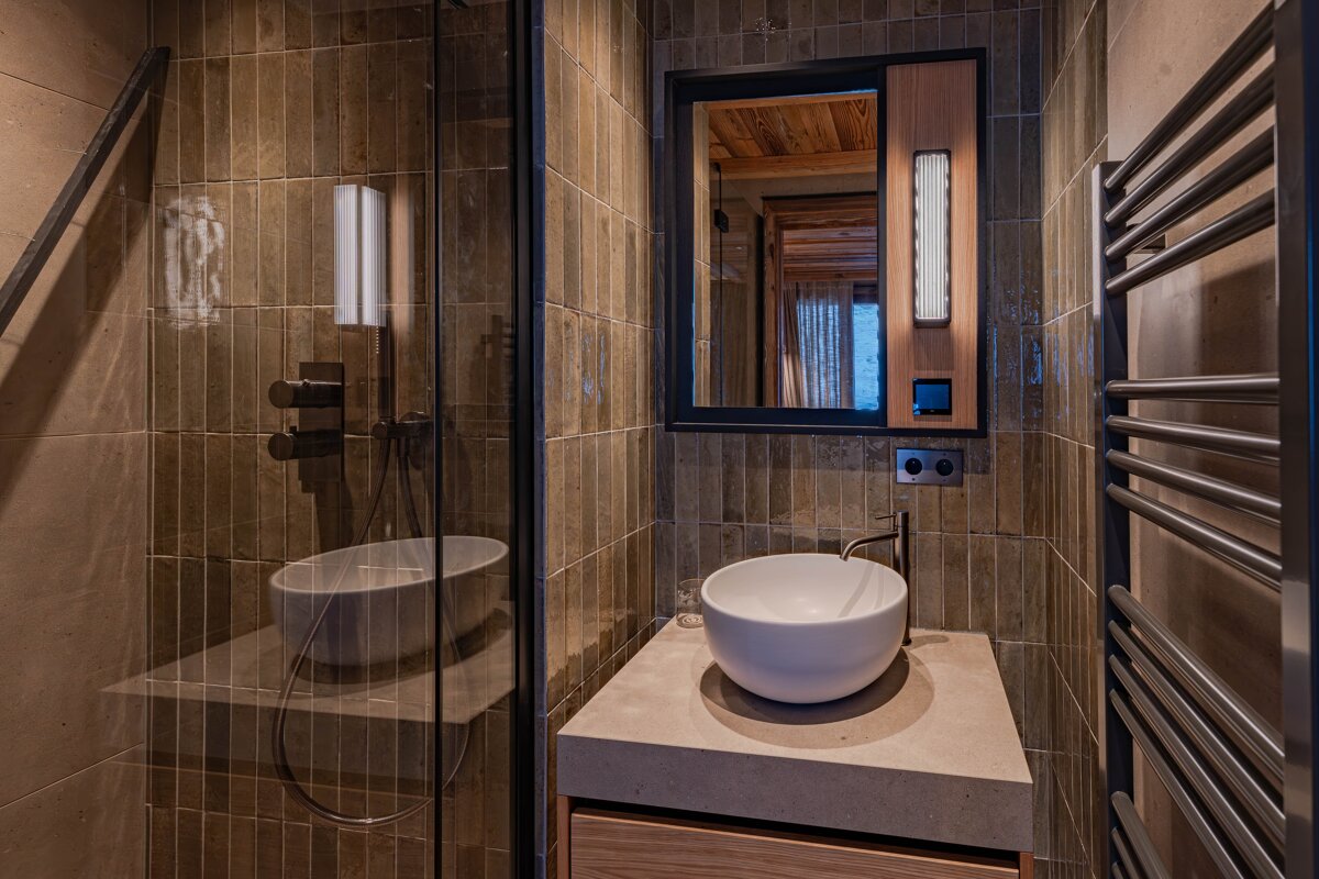 A modern bathroom featuring olive-green tiles, a glass-enclosed shower, a round vessel sink on concrete, and a heated towel rack.