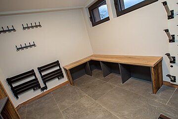 A ski mudroom featuring a wooden corner bench, wall hooks, heated racks, and ski storage brackets.