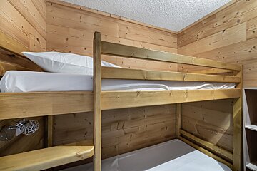 A bunk bed in a wooden room with white sheets