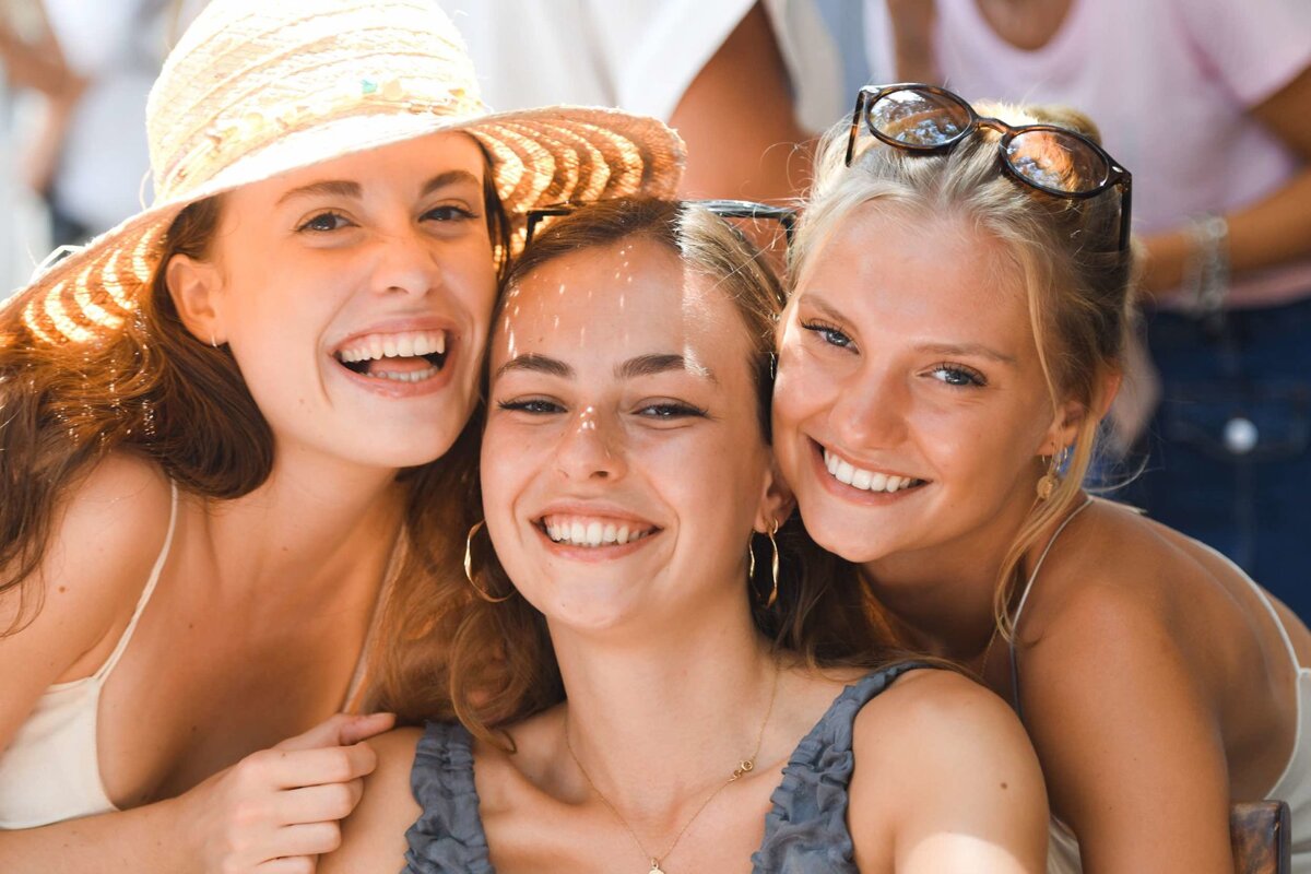 Three women are posing for a picture and one is wearing a hat