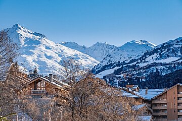 Snowy mountain ski resort with cozy wooden chalets and bare trees under a clear blue sky.