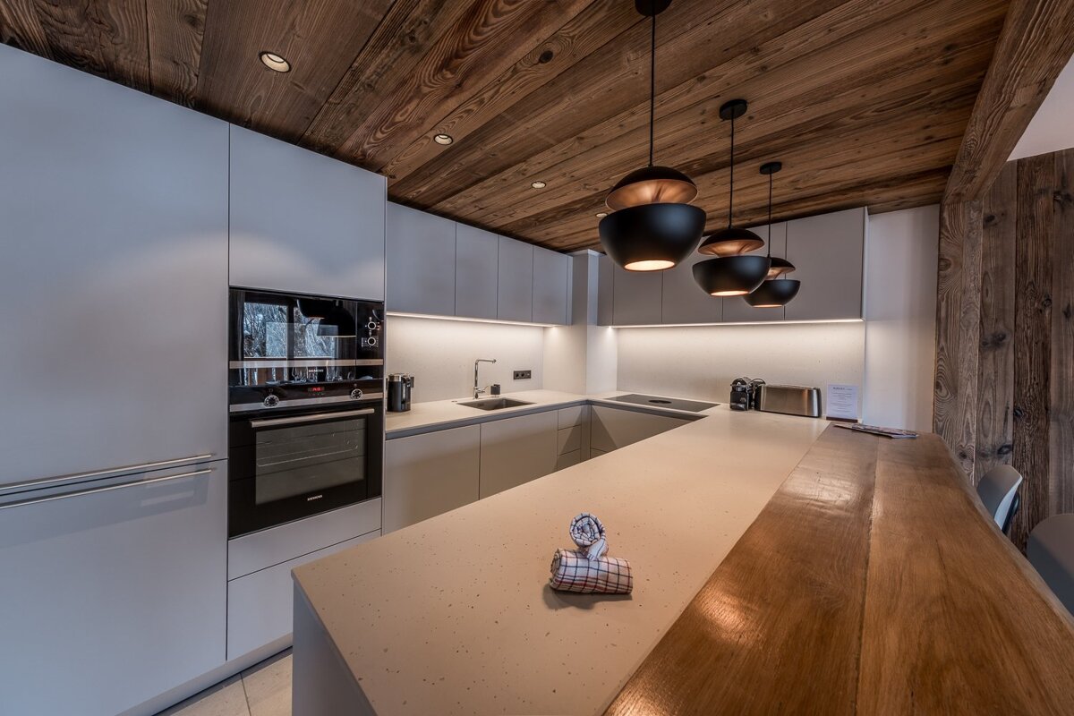 Modern kitchen with white cabinets, a rustic wood ceiling, black pendant lights, and a large island with a wooden bar top.