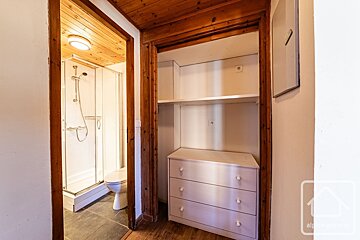 A doorway reveals a bathroom with a shower and toilet, adjacent to an open closet featuring shelves and a three-drawer dresser.