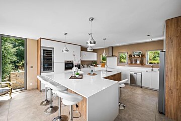 A modern, spacious kitchen featuring white countertops, wooden accents, a large island with bar stools, and ample natural light.