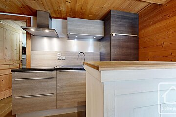 Modern kitchen featuring light wood cabinetry, dark counters, stainless appliances, and warm wood paneling, plus a partial island.