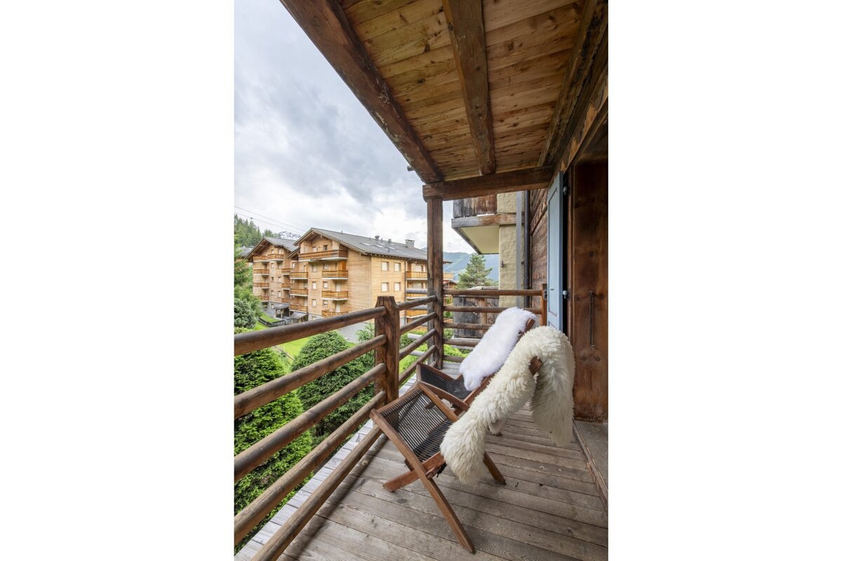 A wooden balcony with a chair and a blanket on it