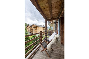A wooden balcony with a chair and a blanket on it