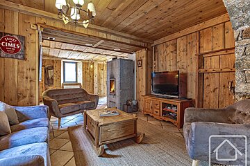 A rustic chalet living room with wood-paneled walls/ceiling, a modern stone fireplace, comfortable sofas, a TV, and a cozy atmosphere.