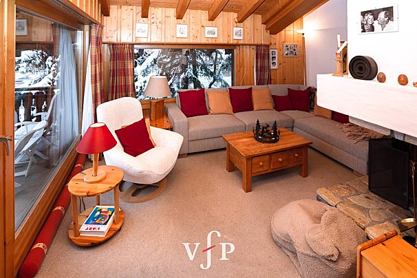 Cozy alpine chalet living room with wood paneling, a large sectional sofa, fireplace, and snowy winter views through the window.