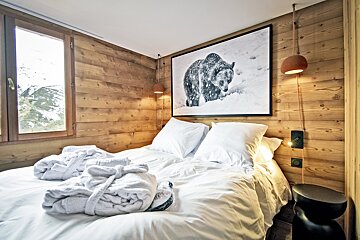 Cozy cabin bedroom with wood-paneled walls, white bedding with folded robes, and a large framed photo of a bear hanging above the bed.