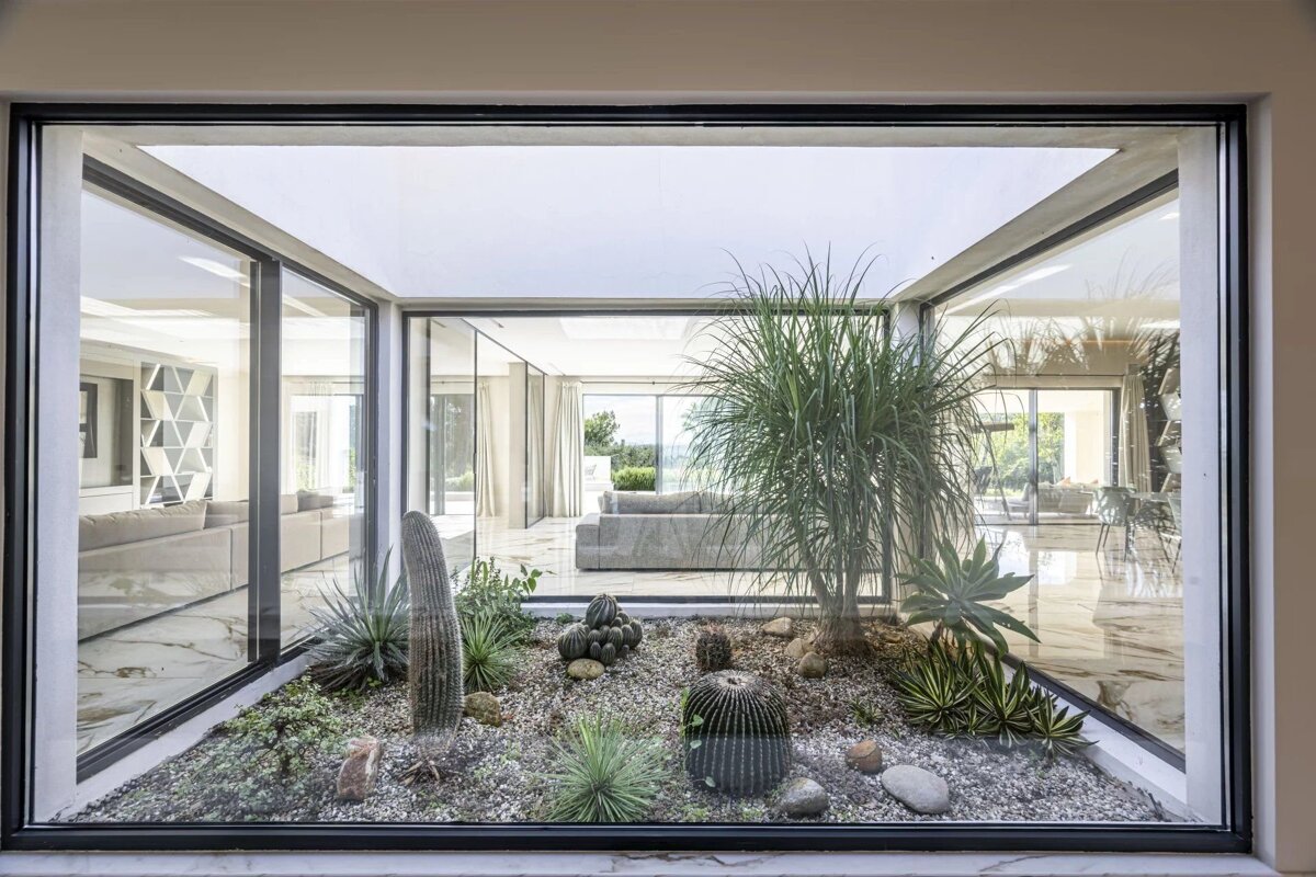 An indoor desert garden with cacti and gravel inside a glass-enclosed atrium of a modern home.