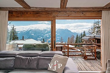 View from a cozy chalet living room overlooking a wooden deck and stunning snow-capped mountains.