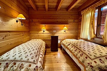 Cozy cabin bedroom featuring two twin beds with floral quilts, warm yellow lighting, and rustic wood walls.