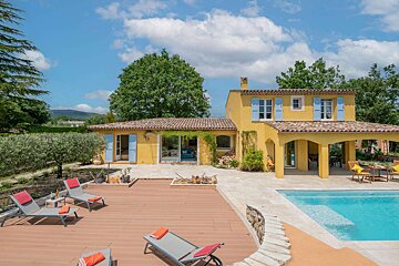 A yellow house with blue shutters sits next to a swimming pool