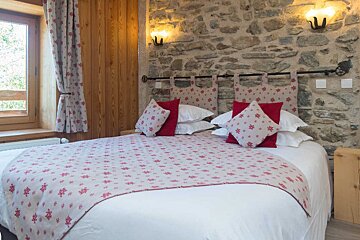 A bedroom with a stone wall and a bed with red pillows