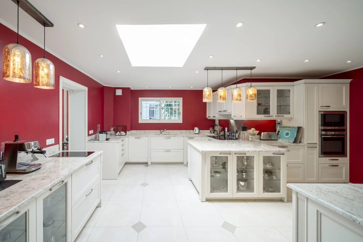 Modern kitchen with bold red walls, white cabinetry, marble countertops, a central island, and elegant pendant lighting.