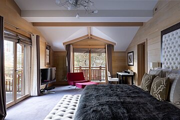 Luxurious, wood-paneled bedroom with a large bed, red accent chair, and a balcony looking out to snowy trees.