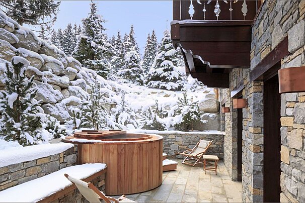 A wooden hot tub is surrounded by snow covered trees