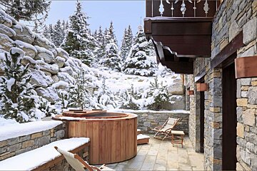 A wooden hot tub is surrounded by snow covered trees