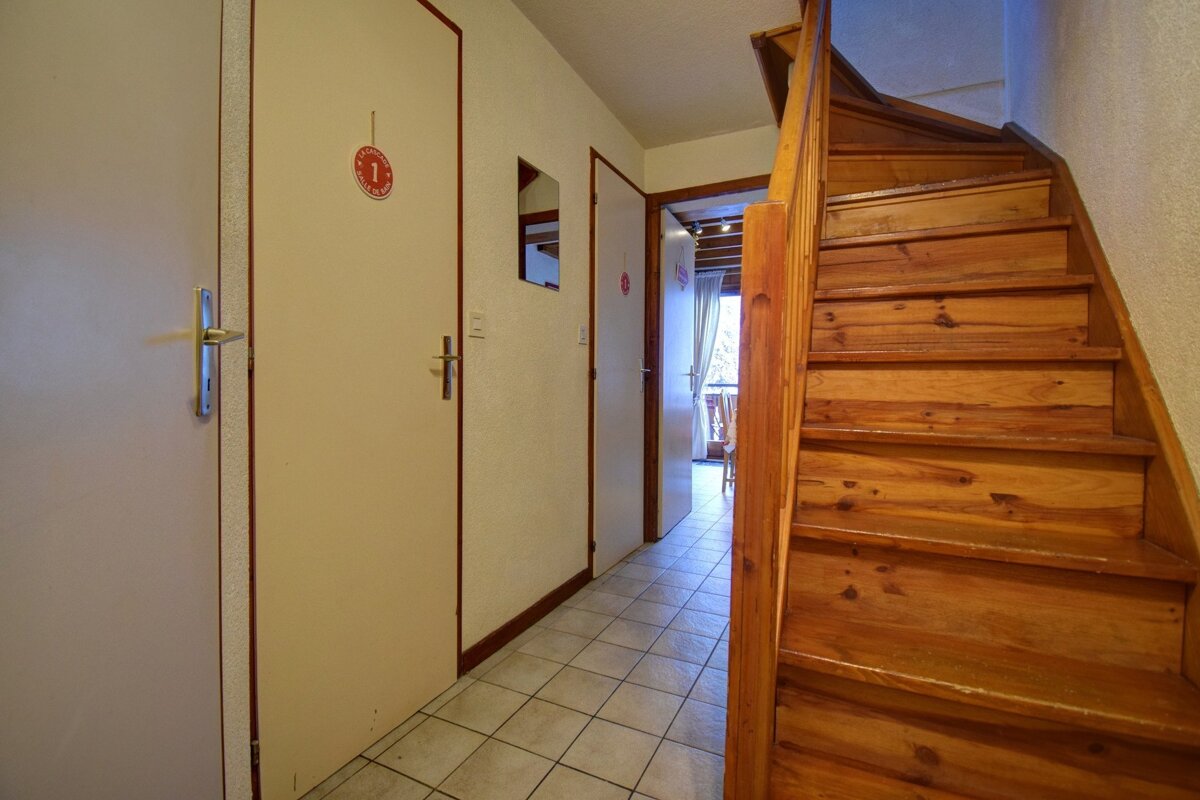 A hallway with tiled flooring, beige doors on the left, and a wooden staircase on the right.