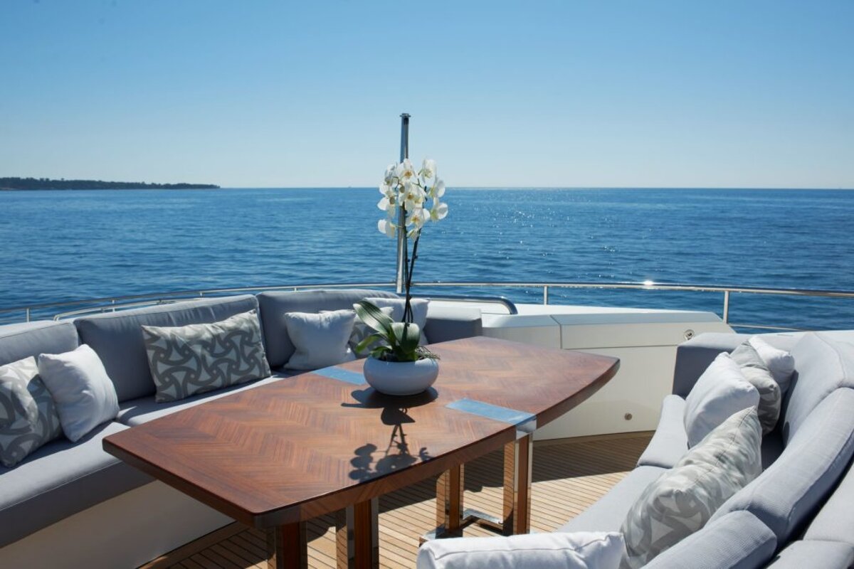 A table with a vase of flowers on it sits on the deck of a boat overlooking the ocean