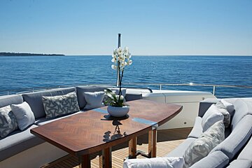 A table with a vase of flowers on it sits on the deck of a boat overlooking the ocean