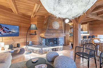 Cozy wooden chalet living room featuring a stone fireplace, a TV, unique spherical lighting, and modern furniture.