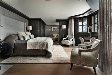 A luxurious bedroom with dark wood, a plush bed, two armchairs, and a snowy view. Cozy and sophisticated ambiance.