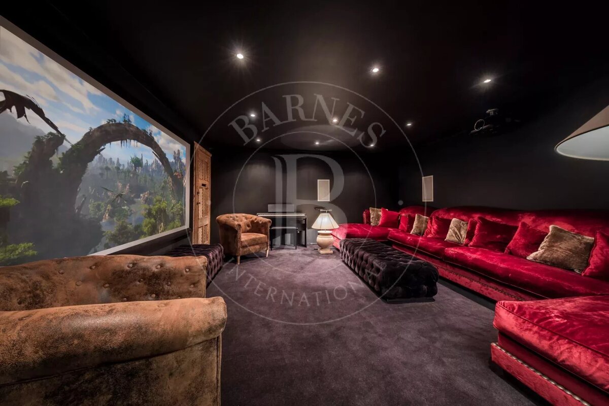 A luxurious home cinema with a massive screen displaying a fantasy landscape, featuring plush red velvet sofas, brown armchairs, and dark decor.
