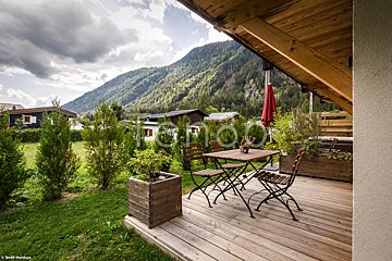 A wooden deck with a table and chairs and a mountain in the background