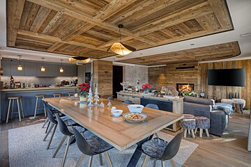 Luxurious open-plan chalet with rustic wood features, a modern kitchen, large dining table, and a cozy living area with a fireplace.