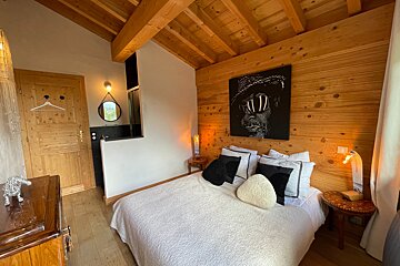 A rustic modern bedroom with wooden walls and ceiling, a white bed, and striking black & white art. A partial bathroom and warm lighting complete the cozy space.
